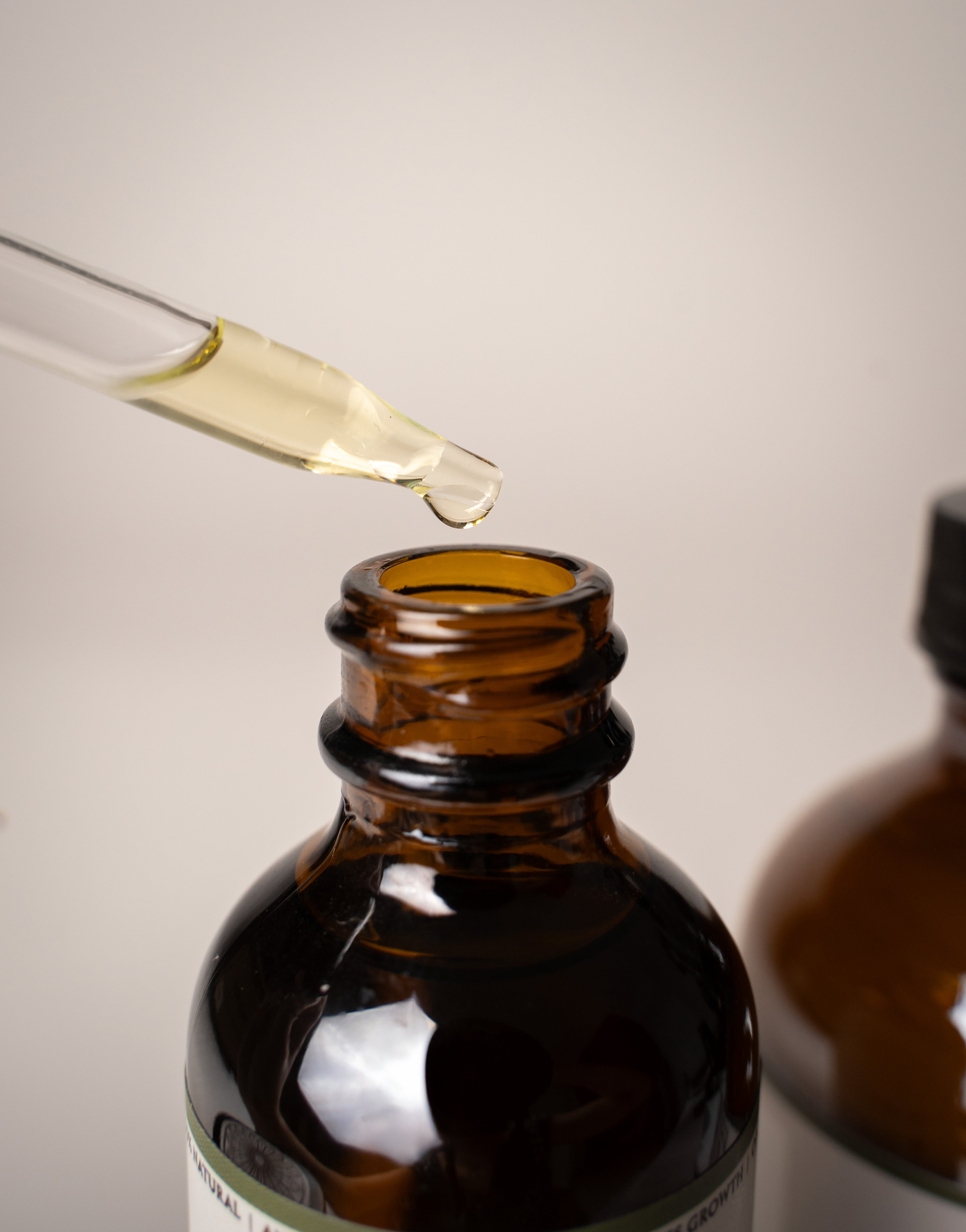 Brown glass dropper bottle with a close-up of the dropper on a light gray background