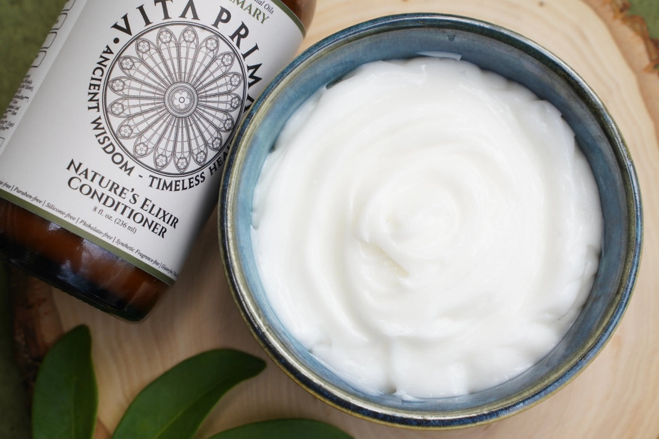 Vita Prim conditioner bottle next to a jar of white cream on a wooden surface with green leaves.