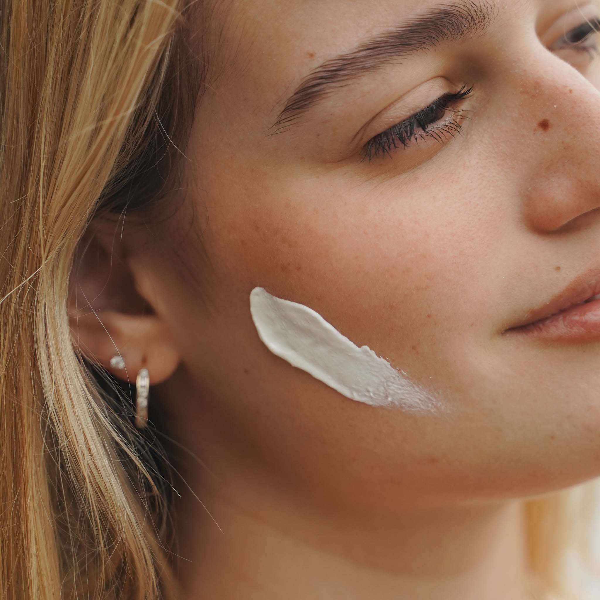 Close-up of a woman's face with a small amount of cream applied to her cheek.